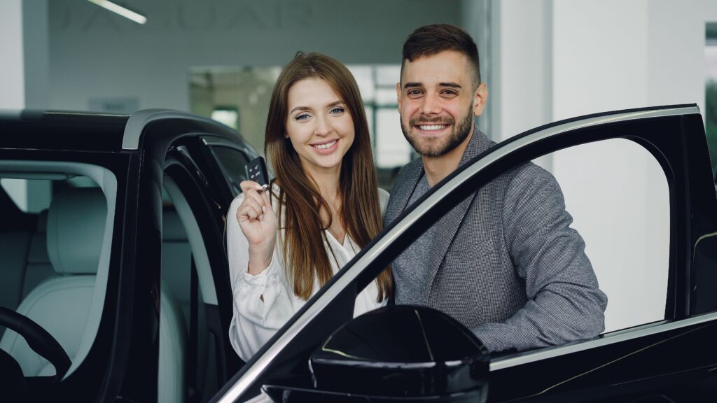 A cheerful couple in a car showroom holding car keys, symbolizing a new purchase.